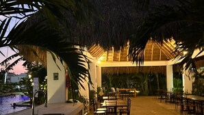 An outdoor dining area with tables and chairs, a pool, and a thatched-roof structure. - First Floor*Coto*Pool*AC*TV*WiFi*10 min to Bucerías* (Aldea Hortus)