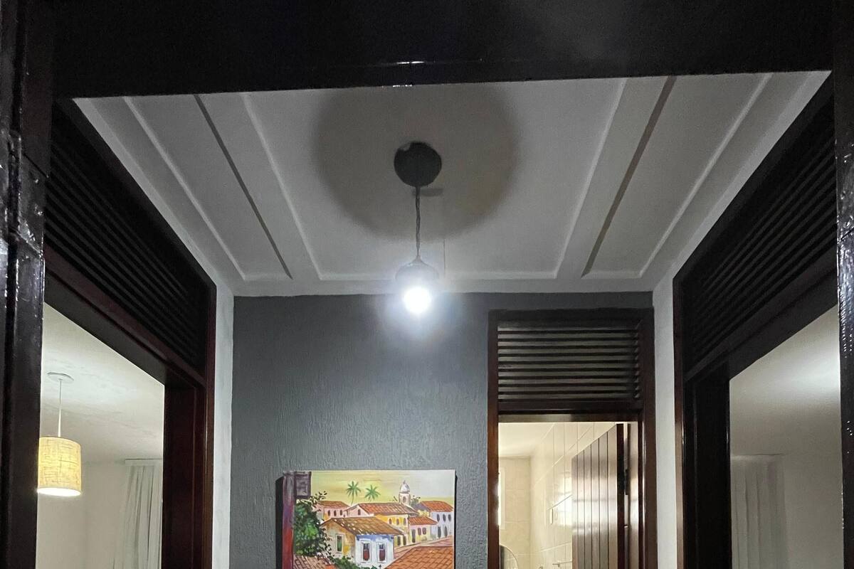 Un couloir orné d’un tableau représentant une scène de ville, avec un luminaire au plafond et une porte donnant sur une chambre à coucher.