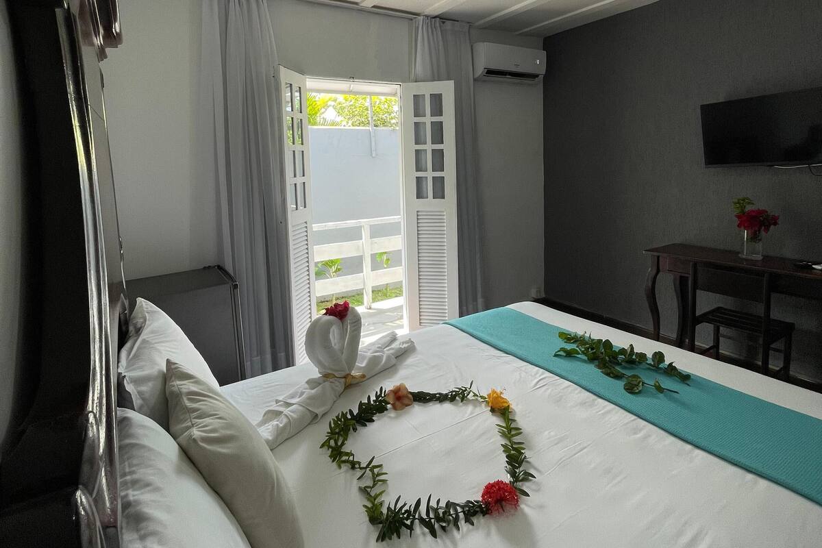 Une chambre d’hôtel avec un lit bien fait, un téléviseur fixé au mur et un balcon avec des rideaux.