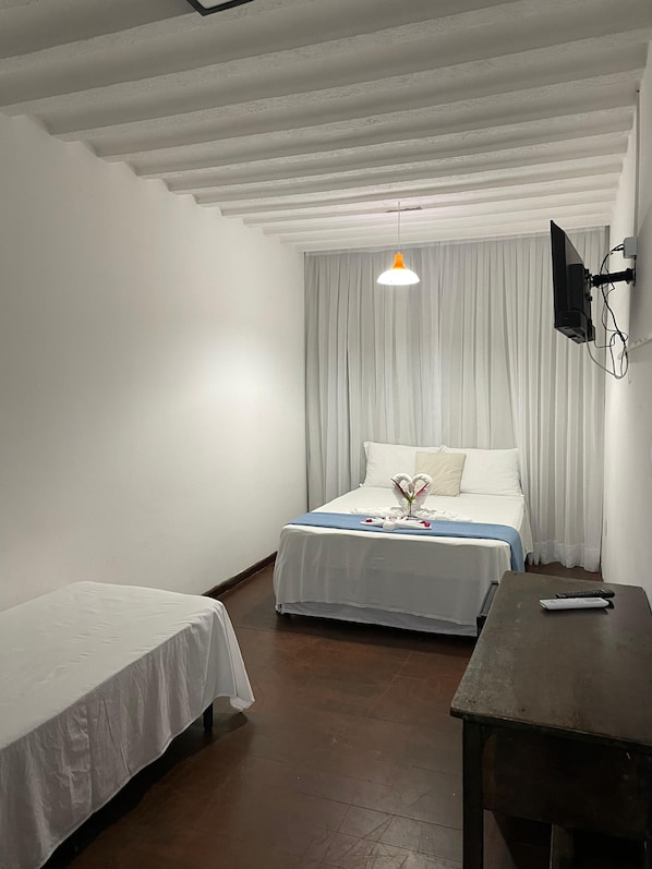 Habitación de hotel con dos camas individuales, una mesa de madera, un televisor montado en la pared y un techo con vigas a la vista.