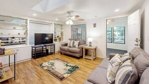 Ein Wohnzimmer mit einer Couch, einem Couchtisch, einem Fernseher und einem Deckenventilator.