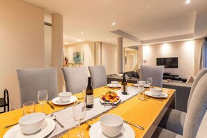A dining area with a long table set for six, including plates, bowls, wine glasses, and a bottle. There are grey upholstered chairs around the table. - Sunset Azure Penthouse - Panoramic Views, PVT Pool (Cape Town)