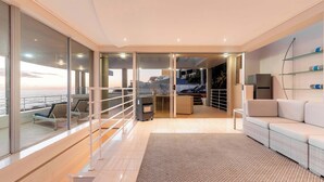 A modern interior with a balcony, a sofa, a kitchen area, and a view of the sea. - Sunset Azure Penthouse - Panoramic Views, PVT Pool (Cape Town)