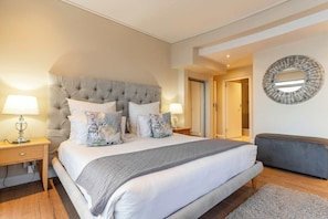A bedroom with a large bed, bedside lamps, a round mirror, and a bench.