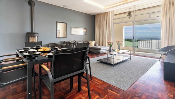 A modern living room with a dining area, a fireplace, a sofa, and a balcony with a view. - 5 min walk to Camps Bay beach, Views - Caprice Bay (Cape Town)