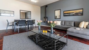 A modern living room with a glass coffee table, grey sofa, and dining area with chairs and a table. - 5 min walk to Camps Bay beach, Views - Caprice Bay (Cape Town)