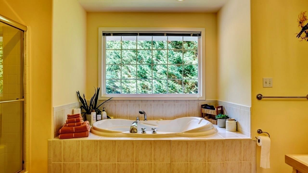Un baño con una bañera grande, una ventana con vistas a árboles y un perchero.