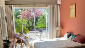 Ein Schlafzimmer mit Bett, Stuhl, Tisch und Blick auf einen Garten durch eine Schiebetür.