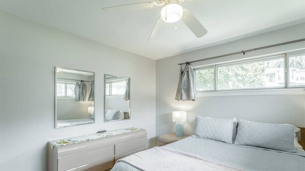 A bedroom with a bed, a dresser, two mirrors, a nightstand, a lamp, and a window with curtains. - Cozy Convenient Mid-Century Apt! (Chattanooga)