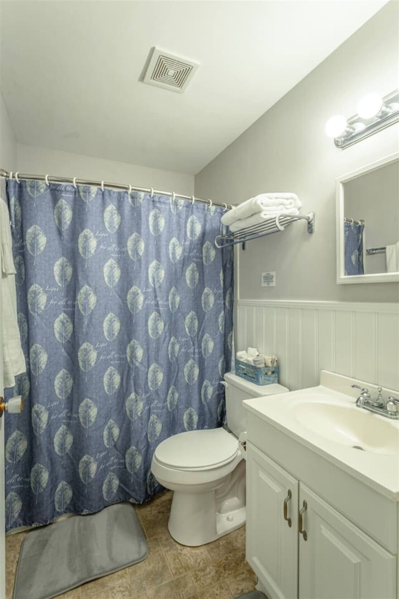 A bathroom with a shower curtain, toilet, sink, and a mirror.