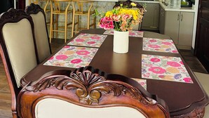 A dining area with a wooden table, chairs, and a vase of flowers. - Casa Jacky (San Salvador)