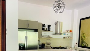 A modern kitchen with a central island, bar stools, a built-in refrigerator, and a hanging light fixture.