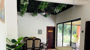A modern living room with a beige sectional sofa, a ceiling fan, and a dining area with wooden furniture. - Casa Jacky (San Salvador)