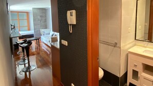 Ein Flur mit Holzboden, einer schwarz gefliesten Wand mit geometrischem Muster, einem weißen Telefon und einem Badezimmer mit weißem Waschbecken und dunkel gefliestem Boden.