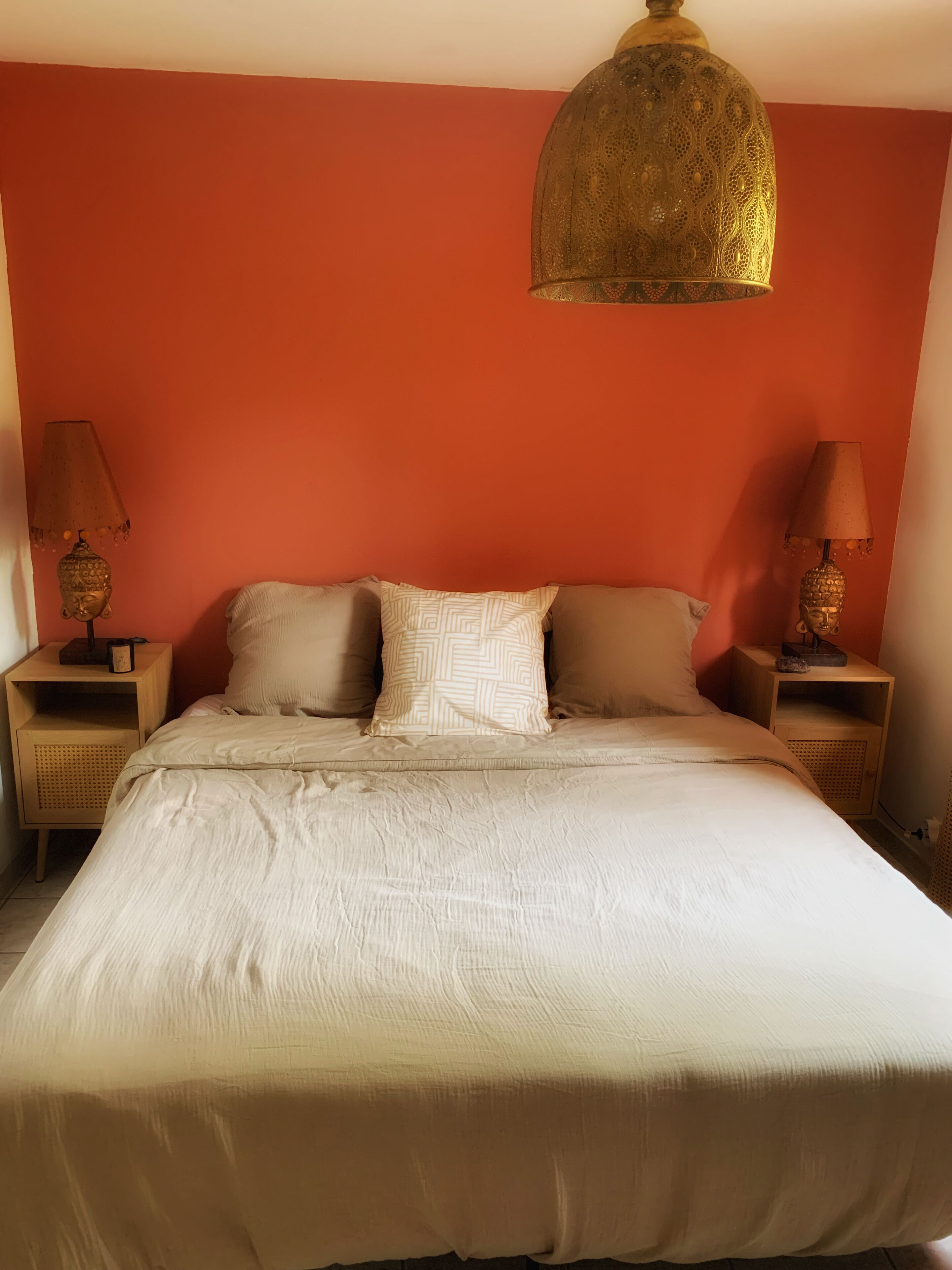 A bed with a beige comforter, two pillows, and a decorative hanging light fixture.