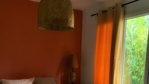 Une chambre à coucher avec un lit, une table de chevet, une lampe et une fenêtre avec des rideaux.