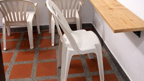 Ein Eckzimmer mit einem Holztisch, zwei weißen Kunststoffstühlen und einem gefliesten Boden.