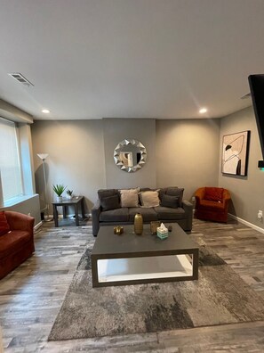 A modern living room with a grey sofa, a coffee table, and a decorative mirror on the wall. - Modern Hyde Park Retreat {Renovated 2BR with Stylish Updates & Prime Location} (St. Louis)