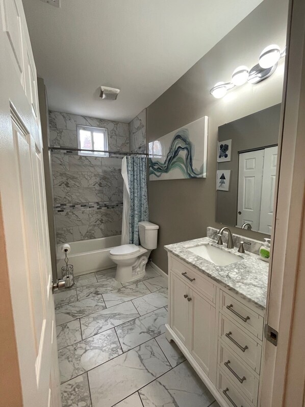 A bathroom with a bathtub, toilet, and vanity with a mirror. - Modern Hyde Park Retreat {Renovated 2BR with Stylish Updates & Prime Location} (St. Louis)