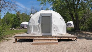 A dome-shaped tent with a door, set on a wooden platform with gravel around it. - Luxe King GeoDome Tobermory Glamping West (Miller Lake)