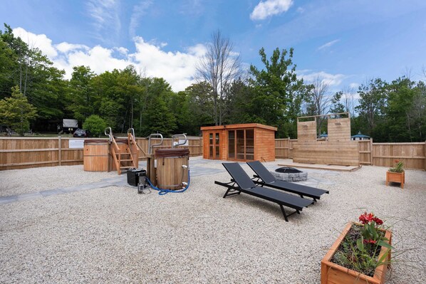 A covered outdoor area with a wooden deck, lounge chairs, a hot tub, and a small wooden structure.