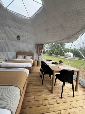 Un interior acogedor con suelo de madera, una cama, una mesa con sillas y vistas al exterior a través de una ventana de diseño geométrico.