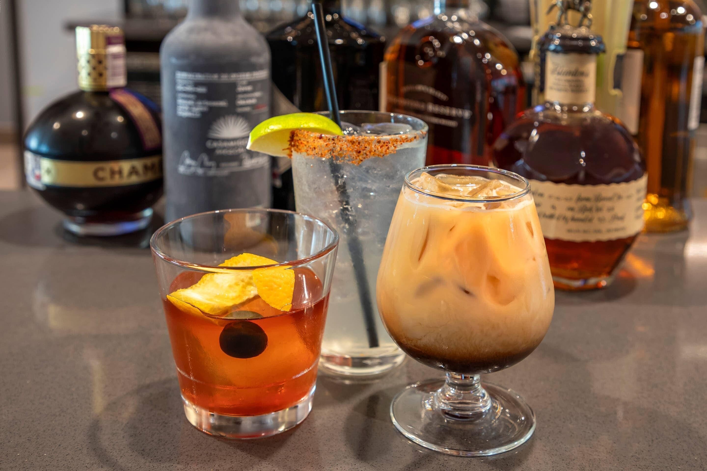 Three different drinks on a bar counter with various bottles in the background.