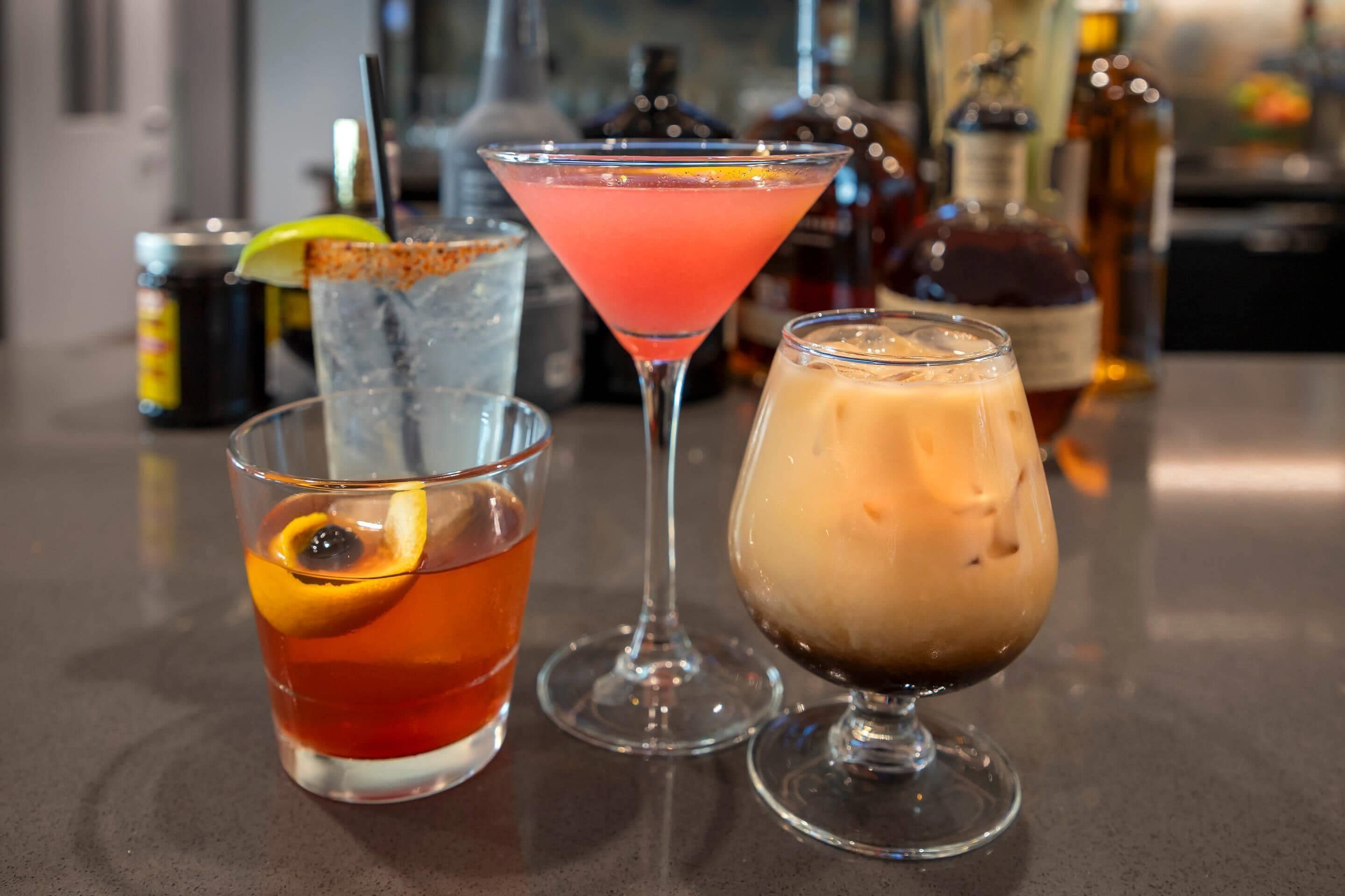 Three different drinks on a bar counter with bottles in the background.