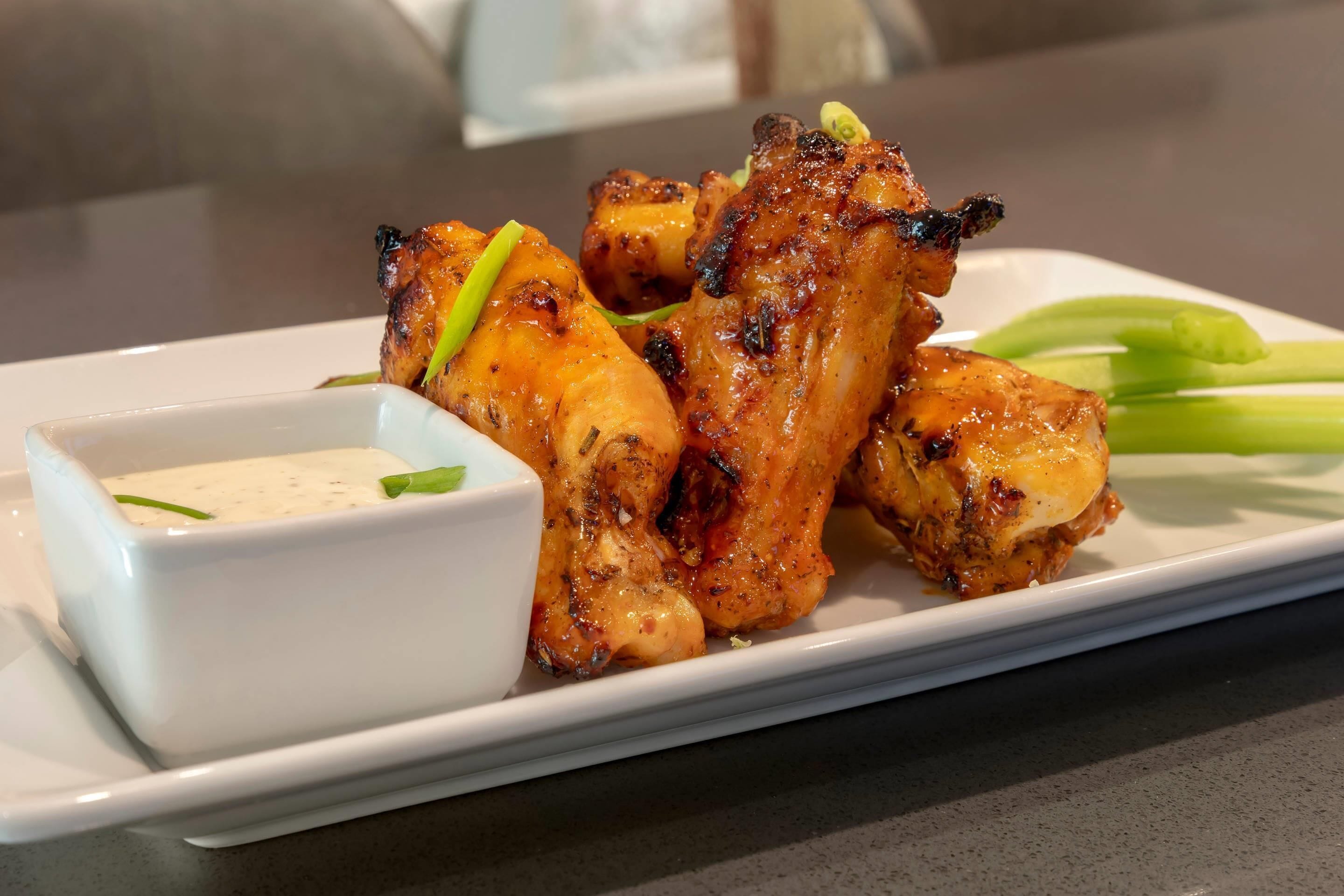 A plate of grilled chicken wings with a side of dipping sauce and celery sticks.