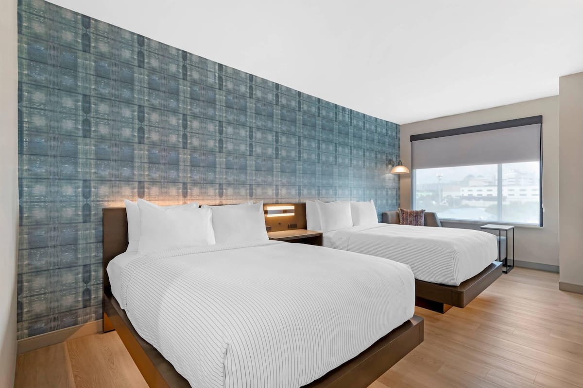 Une chambre d’hôtel moderne avec deux lits, une grande fenêtre et une vue sur la ville.