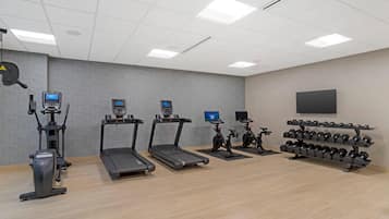 Un gimnasio con cintas de correr, elípticas, bicicletas estáticas y un rack de mancuernas.