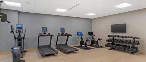 A gym with treadmills, elliptical machines, stationary bikes, and a rack of dumbbells.