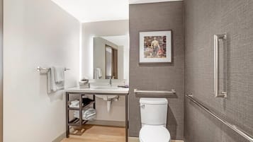 A modern bathroom with a toilet, sink, and mirror. There is a towel rack and a shelf with folded towels.