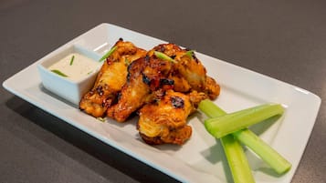 A white rectangular plate with grilled chicken wings, a small bowl of dipping sauce, and celery sticks.