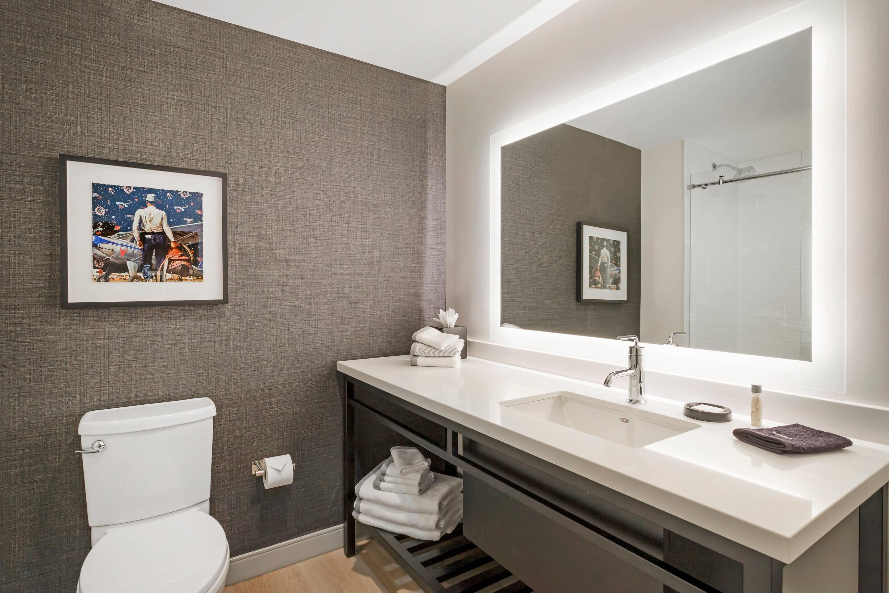 A modern bathroom with a white sink, large mirror, and a framed picture on the wall.