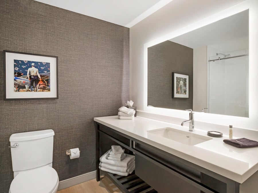 Une salle de bain moderne avec un lavabo blanc, un grand miroir et un tableau encadré au mur.