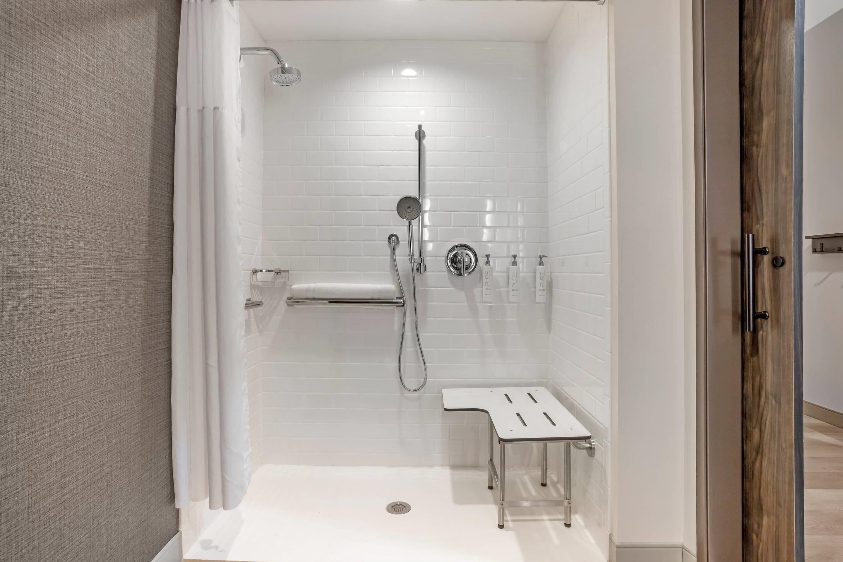 A modern shower area with a glass door, a handheld showerhead, a wall-mounted faucet, and a small bench.