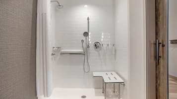 A modern shower area with a glass door, a handheld showerhead, a wall-mounted faucet, and a small bench.