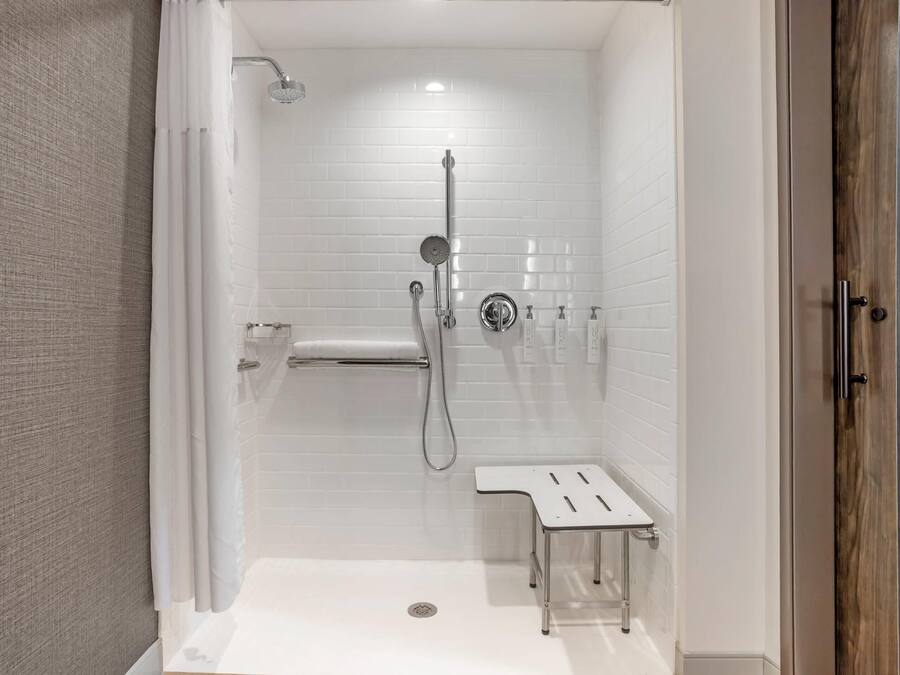 A modern shower area with a glass door, a handheld showerhead, a wall-mounted faucet, and a small bench.