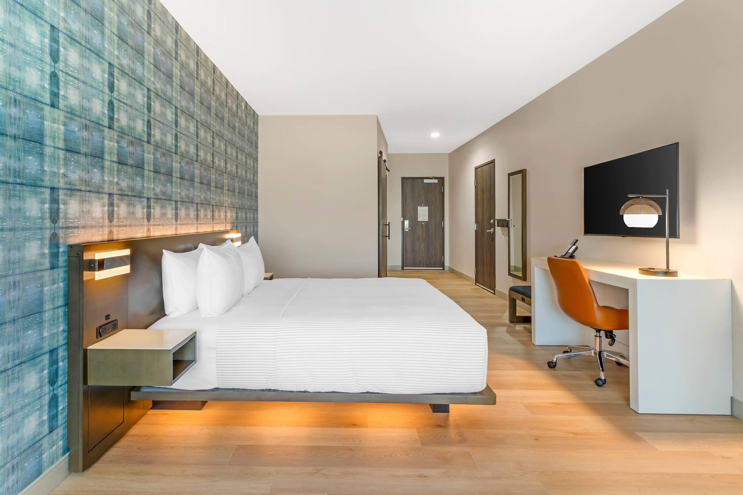 A modern hotel room with a large bed, bedside tables, a desk with an office chair, and a television mounted on the wall.