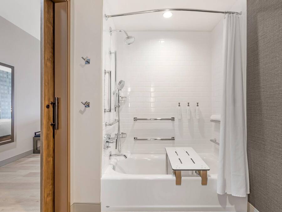 Un baño moderno con bañera, ducha y un pequeño taburete de madera.
