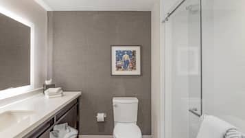 Une salle de bain moderne avec des toilettes blanches, une douche en verre et une œuvre d’art encadrée au mur.