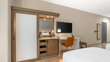 A modern hotel room with a sliding closet, a desk with a chair, a bed, and a TV mounted on the wall.