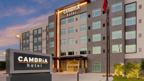 Ein modernes Hotelgebäude mit einem Schild mit der Aufschrift "CAMBRIA hotel" und einem gut beleuchteten Eingang.