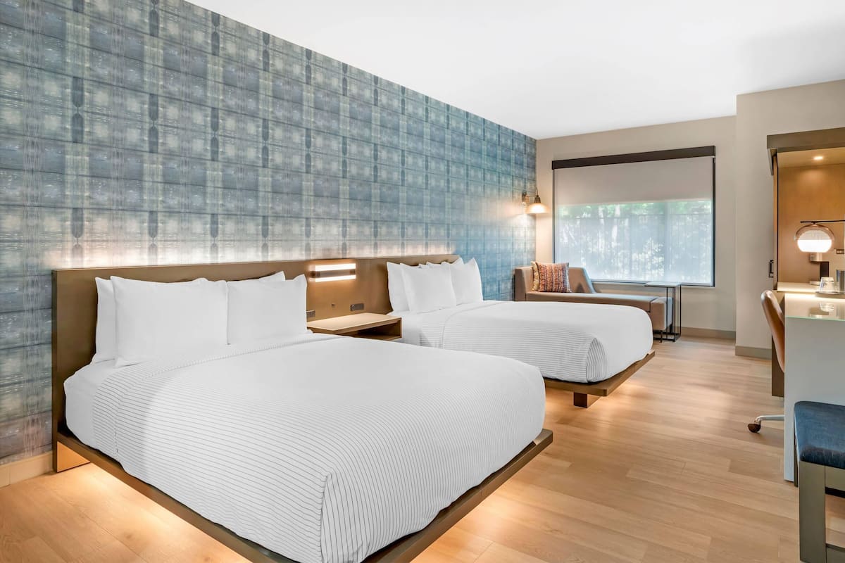 Une chambre d’hôtel avec deux lits, un bureau et une fenêtre donnant sur un espace verdoyant.