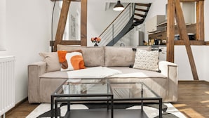 A living room with a sofa, a glass coffee table, and a wooden ceiling structure.