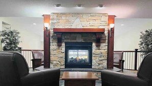 A stone fireplace with a modern design, flanked by two leather armchairs and a small wooden table in a cozy lounge area. - Mountain View Studio with Deck, BBQ & Pool (Fernie)