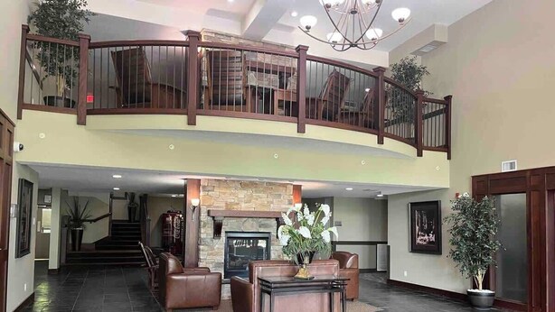 A spacious lobby with a fireplace, leather seating, and a staircase leading to an upper level. - Mountain View Studio with Deck, BBQ & Pool (Fernie)
