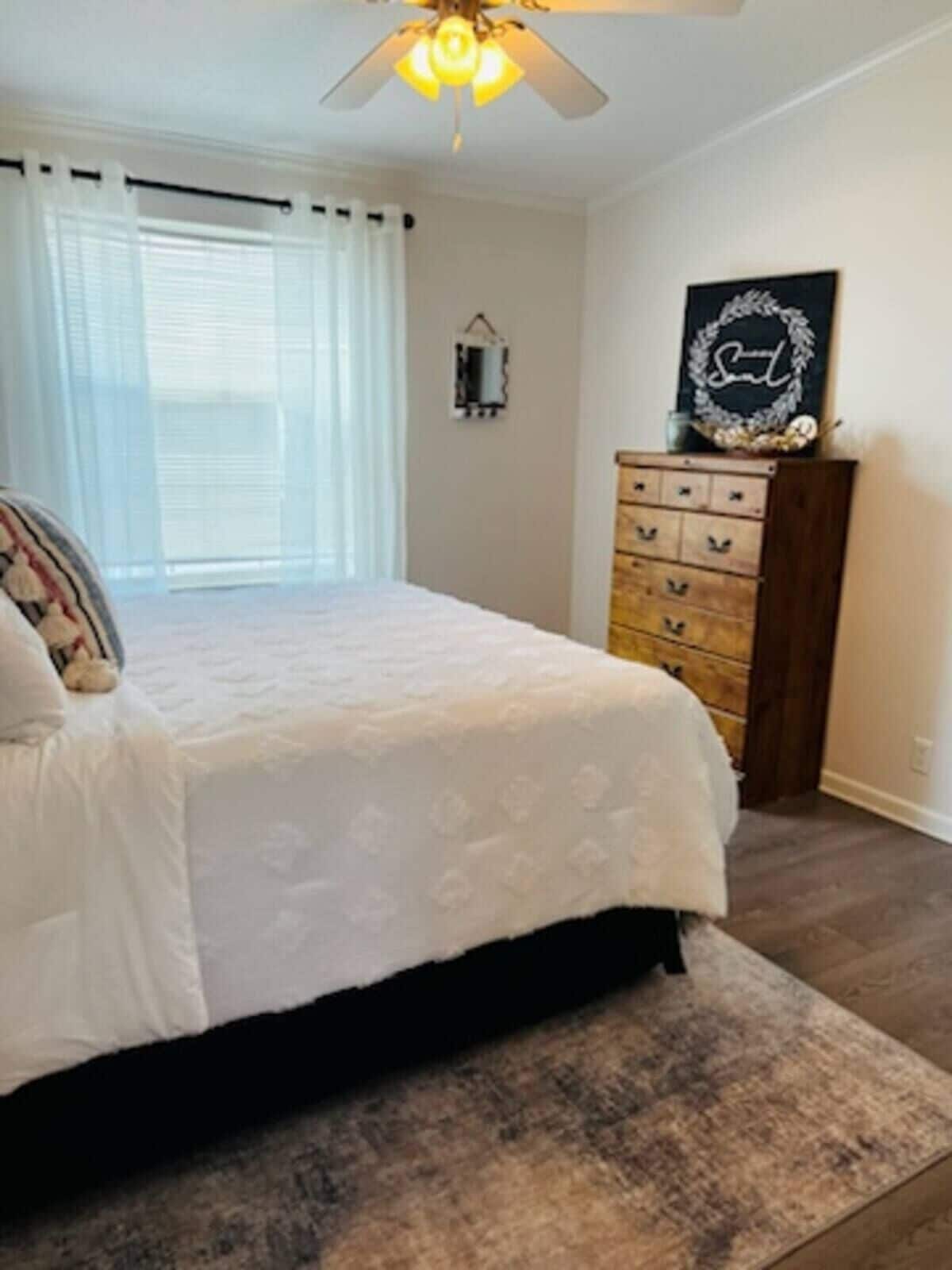 A bedroom with a bed, a dresser, a ceiling fan, and a window with curtains.