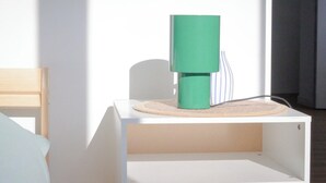 A room with a white bed, a green cylindrical object on a white table, and a wooden chair. - LES LOGIS DU GENERAL - Ground floor apartment (Beaupréau-en-Mauges)
